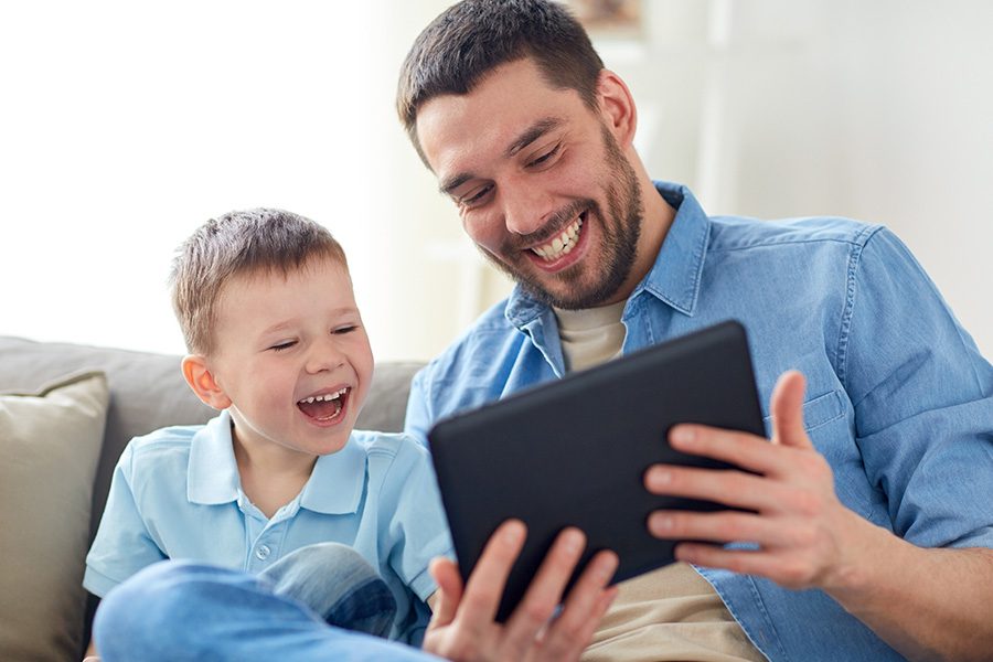 Client Center - Happy Father and Small Son Having Fun Using Their Tablet at Home on the Sofa