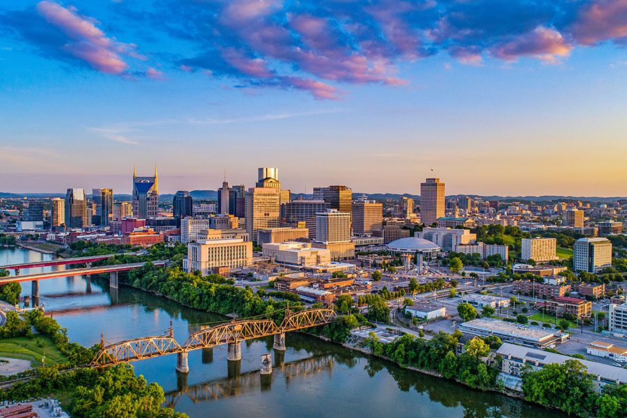 Contact - Long Distance View of Nashville Tennessee TN Skyline Displaying Many Buildings and Bridges That Cross Over a Large River During Sunset