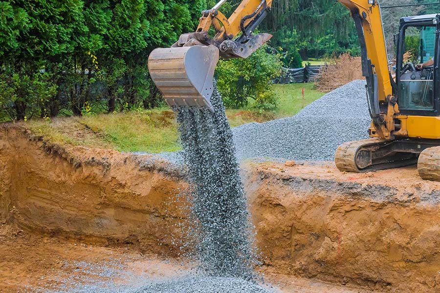 Specialized Business Insurance - View of an Excavator Dropping a Large Amount of Gravel into a Dug Out Foundation Area
