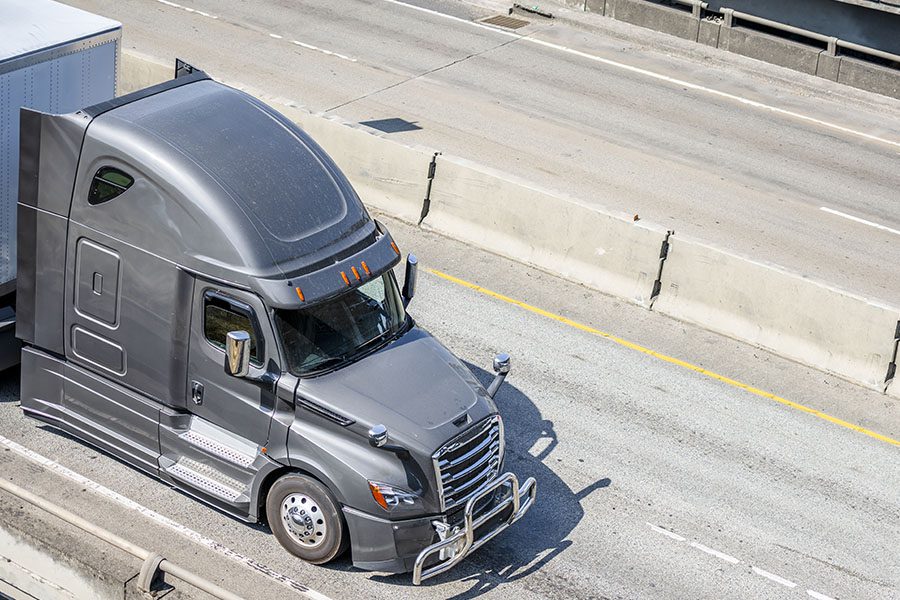 Transport and Delivery Insurance - Aerial View of a Gray Big Rig Long Haul Semi Truck Driving Down a Highway